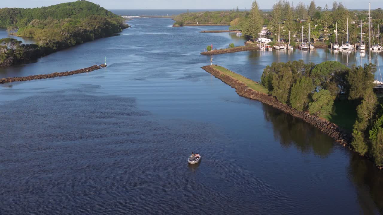 Aerial footage captures serene waterway with boats, lush greenery, and clear skies in Brunswick Heads, NSW, Australia