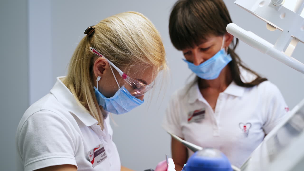 Female medics working in the clinics. Dentist in goggles and mask performing dental care for the patient.