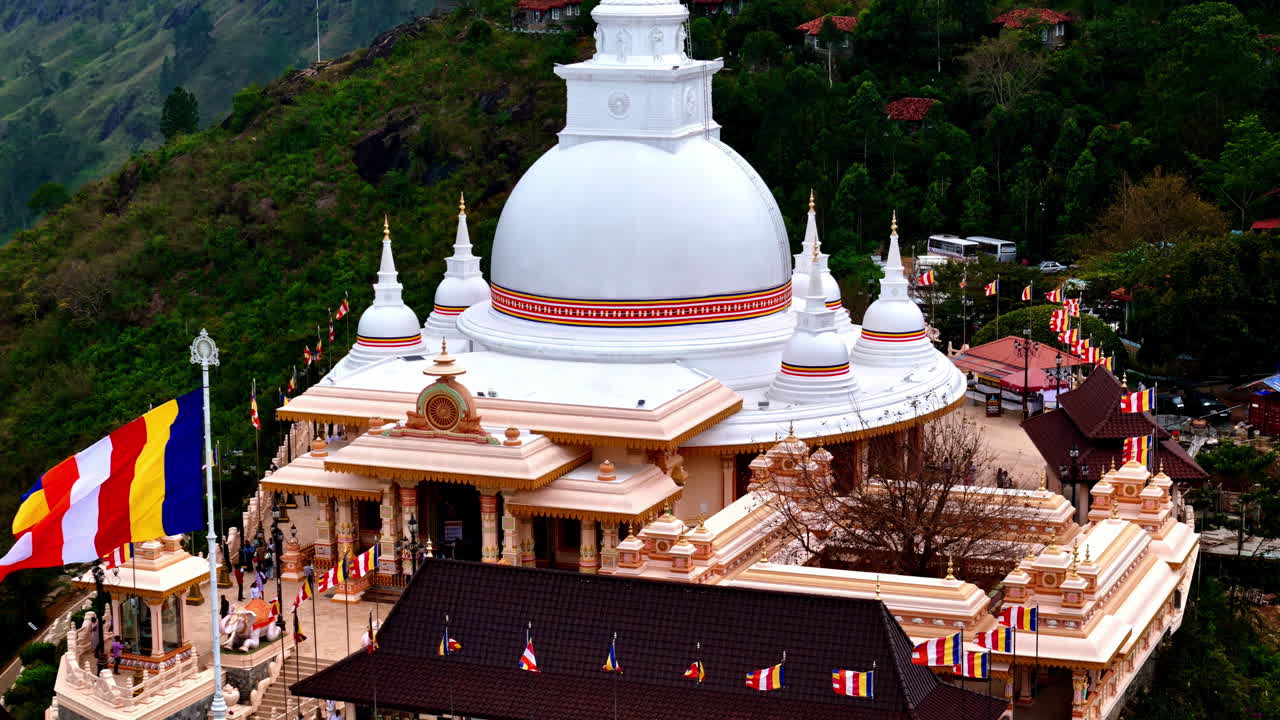 Vista aerea del bianco stupa del monastero buddista Mahamevnawa che si erge sopra le lussureggianti colline dello Sri Lanka, con colorate bandiere di preghiera e tetti di villaggi che creano un pacifico paesaggio spirituale