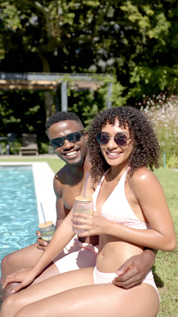 Vertical video: Relaxing by pool, couple in swimwear enjoying drinks and smiling together
