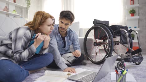 A-student-with-a-disability-and-a-young-girl-look-at-a-laptop-and-books-at-home.