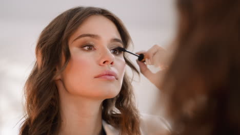 focused woman applies black mascara on eyelashes with wand