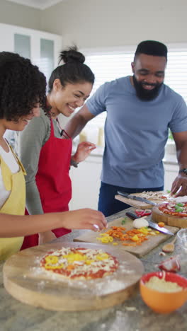 vertical video of diverse male and female friends making pizza in kitchen in slow motion