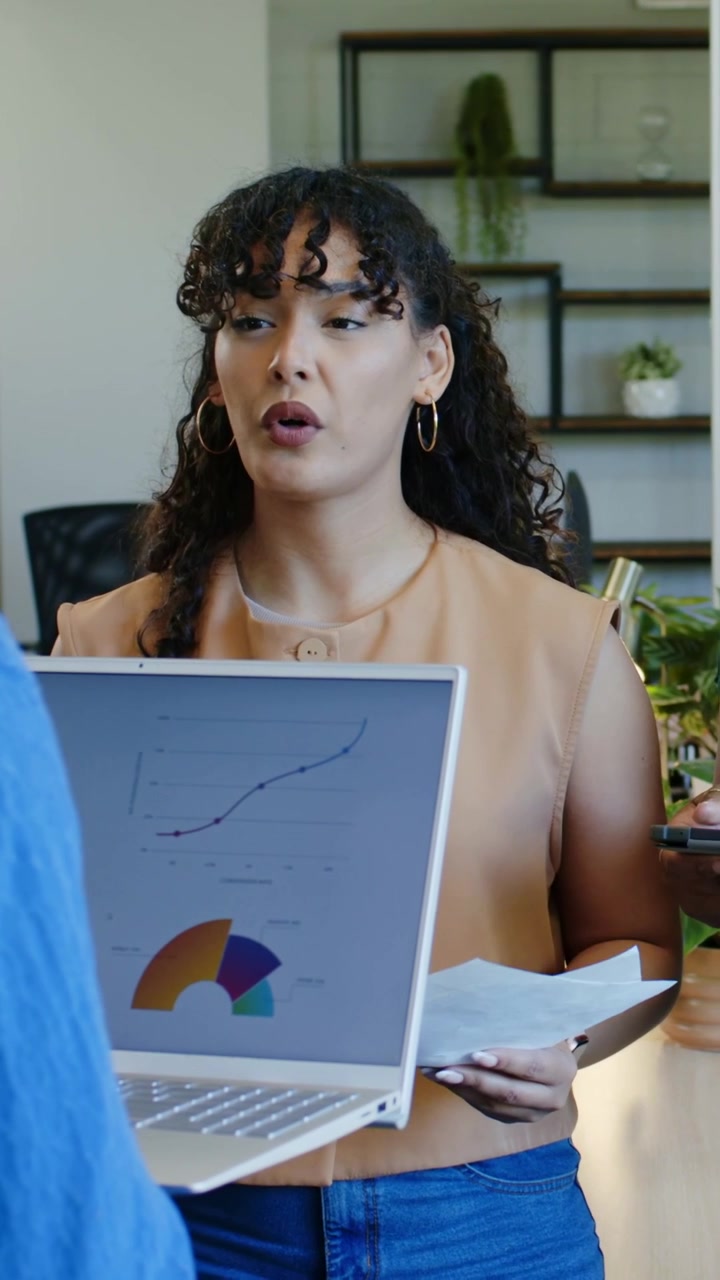 Vertical video: Showing woman in top holding laptop, pages at office after pause, explaining charts