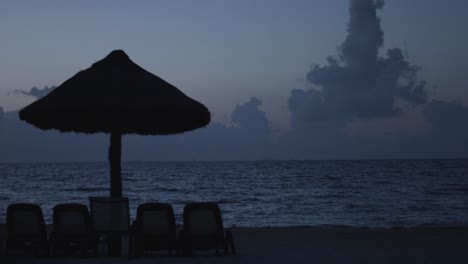 Beach-chairs-and-straw-umbrella-on-seashore-at-dusk