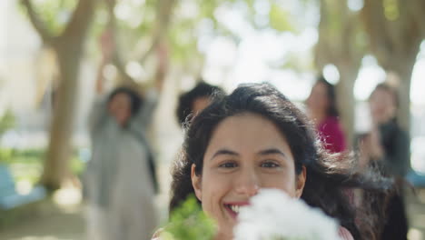 happy bridesmaid showing flower bouquet at the camera during a wedding party in te park