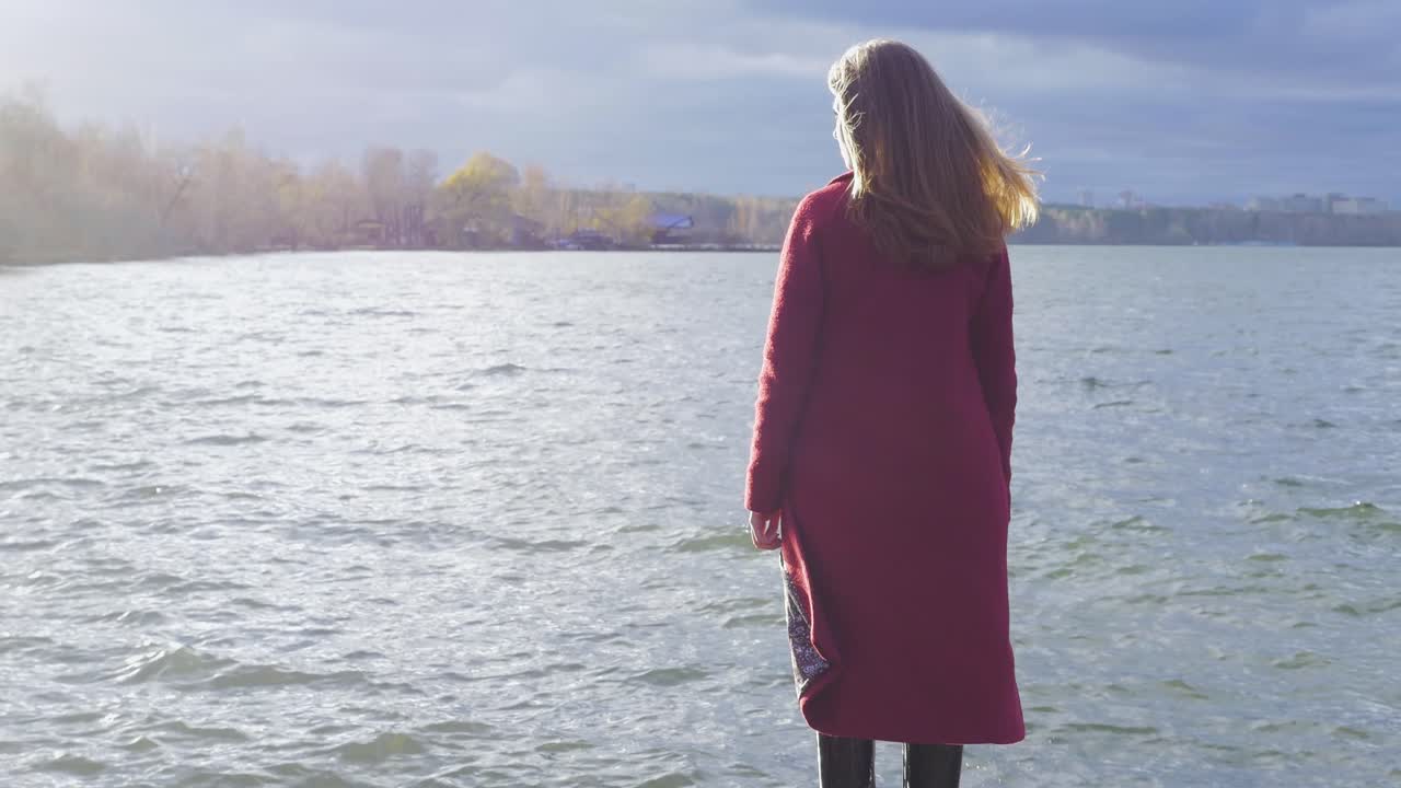 Nainen punaisessa takissa joen rannalla