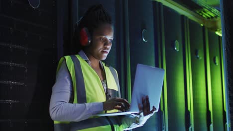 African-american-female-computer-technician-using-laptop-working-in-business-server-room