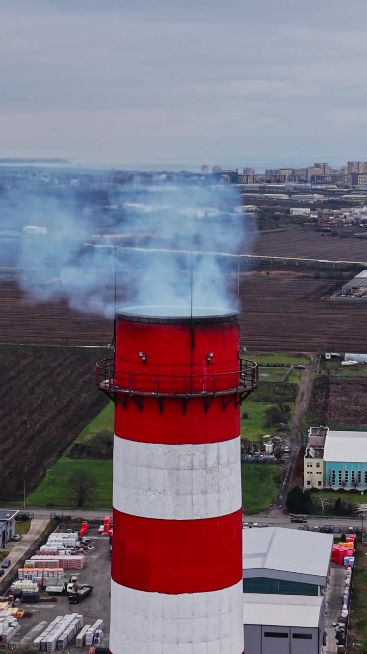Ciminiera industriale che rilascia fumo su un paesaggio urbano in primavera