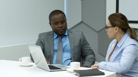 businesswoman and african businessman speaking at table with laptop