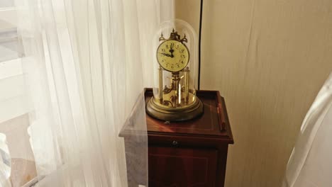 antique table clock inside a glass dome on a table in a room with lots of natural light