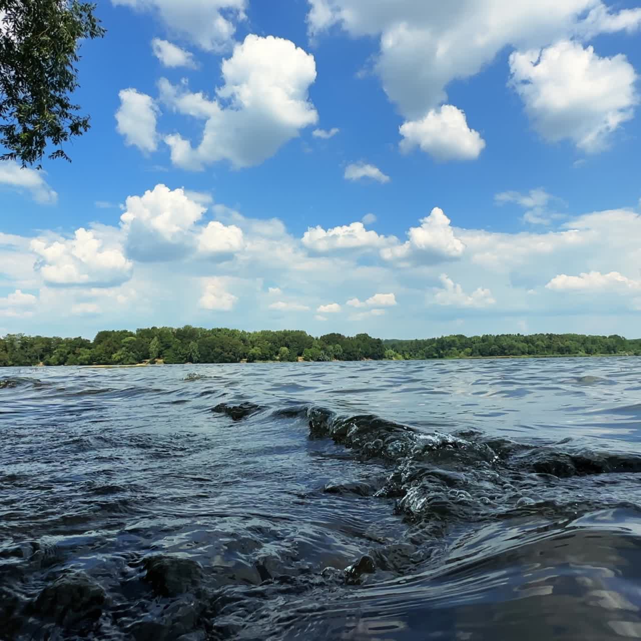 Waves rolling to the stones sticking out of the water. Blue sky with fluffy white clouds low angle view