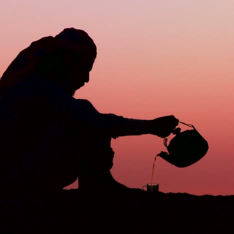 Un-Hombre-Beduino-Vierte-Té-En-Silueta-Contra-La-Atardecer-2