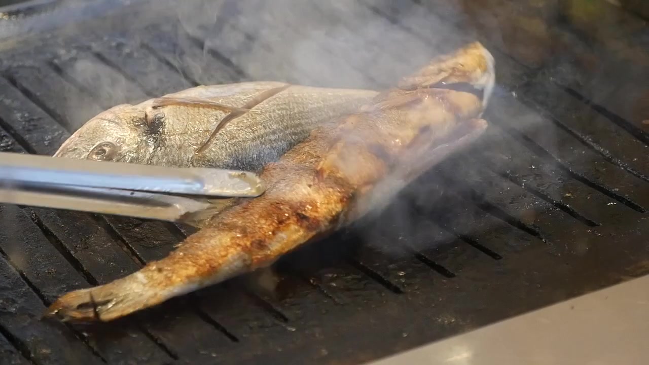 Capovolgere pesce fresco su una griglia rovente.