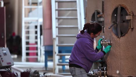 Foto-De-Teleobjetivo-De-Una-Trabajadora-De-Bodega-Comprueba-Un-Indicador-En-Un-Tanque-De-Acero-Inoxidable