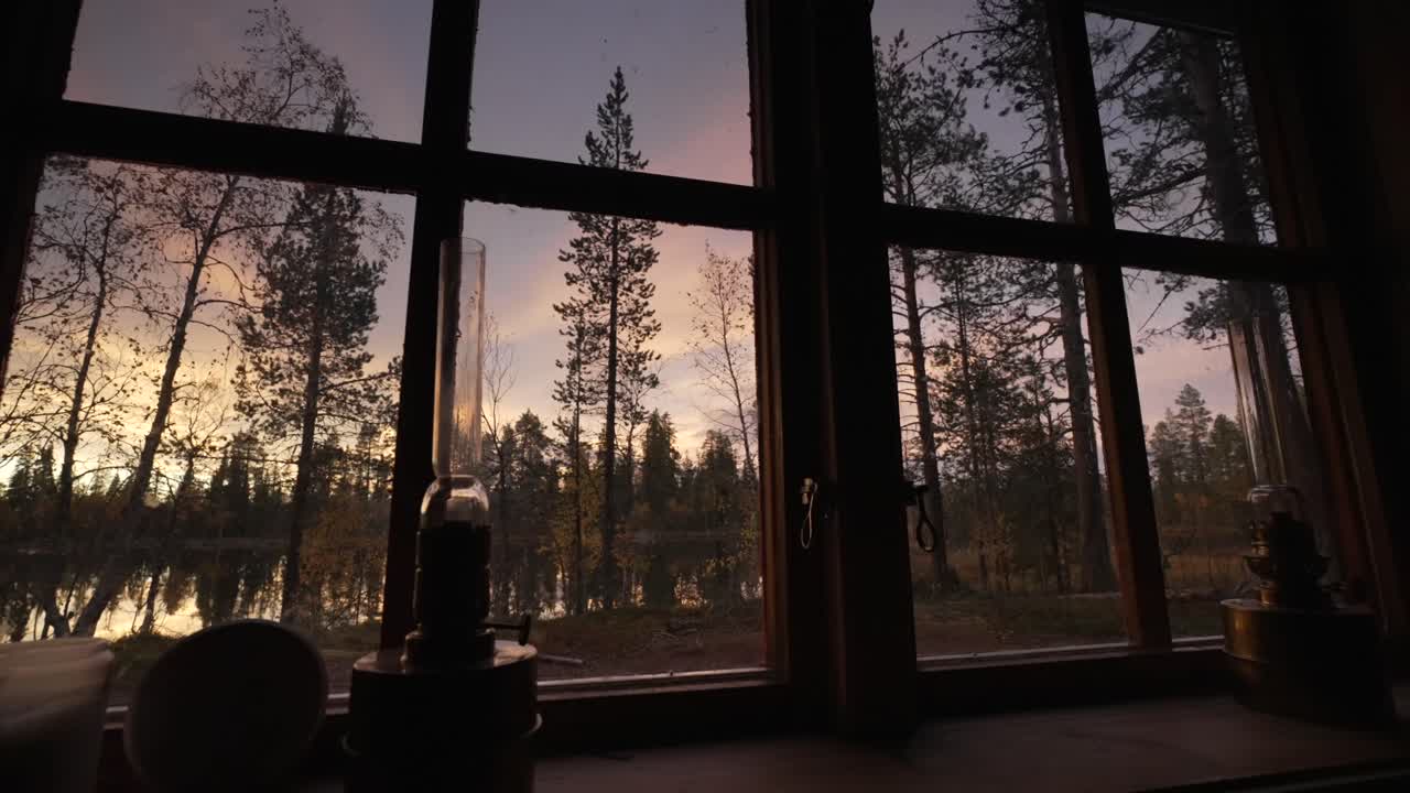 Cabin window frame with view of pine forest and lake at sunset, Nammavarre, Lapland, Sweden