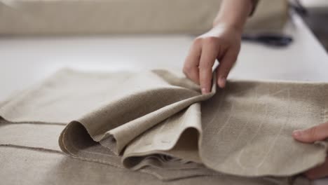 unrecognizable female tailor working with beige fabric patterns at the studio