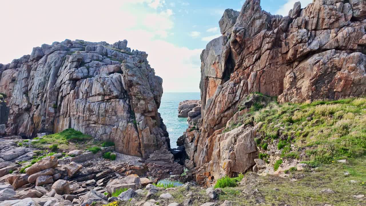 Camera moves backward from the Gouffre de Plougrescant, revealing two towering rock formations and the sea in the background
