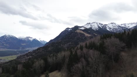 Drone-orbit-above-forest-and-reveal-view-over-cityscape-surrounded-by-mountains-in-Nenzing,-Austria