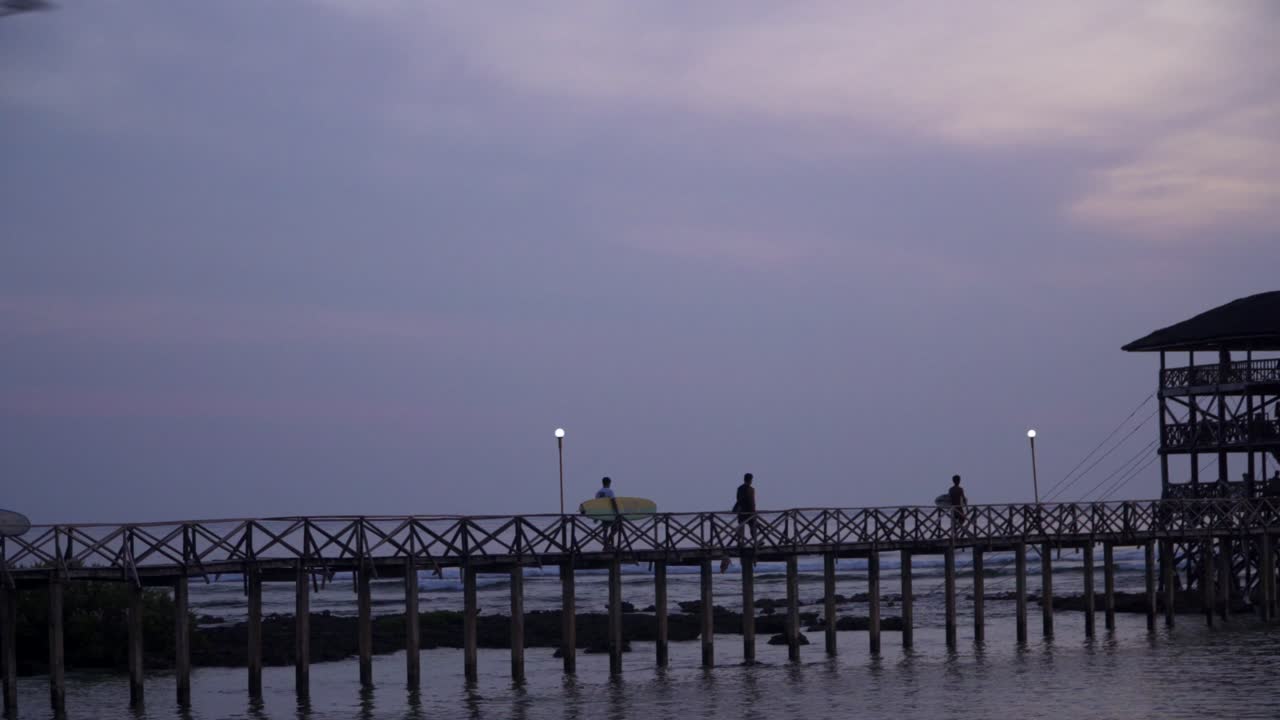 Tracking shot of surfers walking across the Cloud9 boardwalk with the sun low and out of frame, silhouetted against a cloudy sky, filmed in UHD 4K