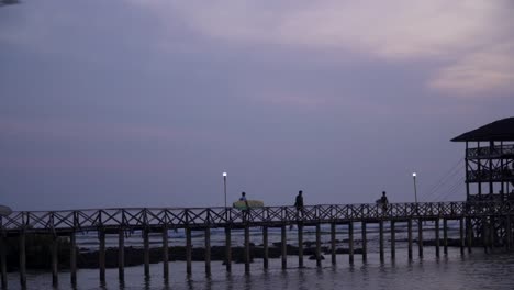 tracking shot of surfers walking across the cloud9 boardwalk with the sun low and out of frame, silhouetted against a cloudy sky, filmed in uhd 4k