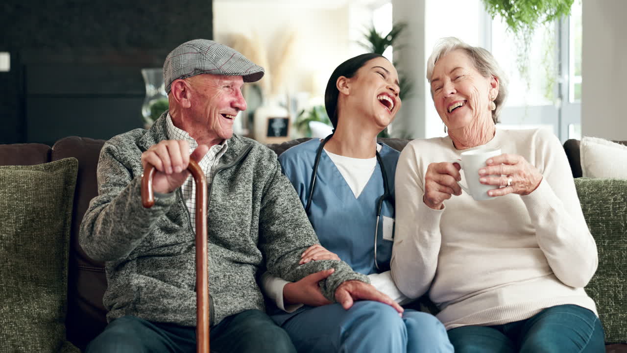 Elderly couple laughing with their nurse on the couch