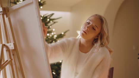 hermosa artista femenina pintando una imagen en lienzo y mezclando colores en una habitación acogedora