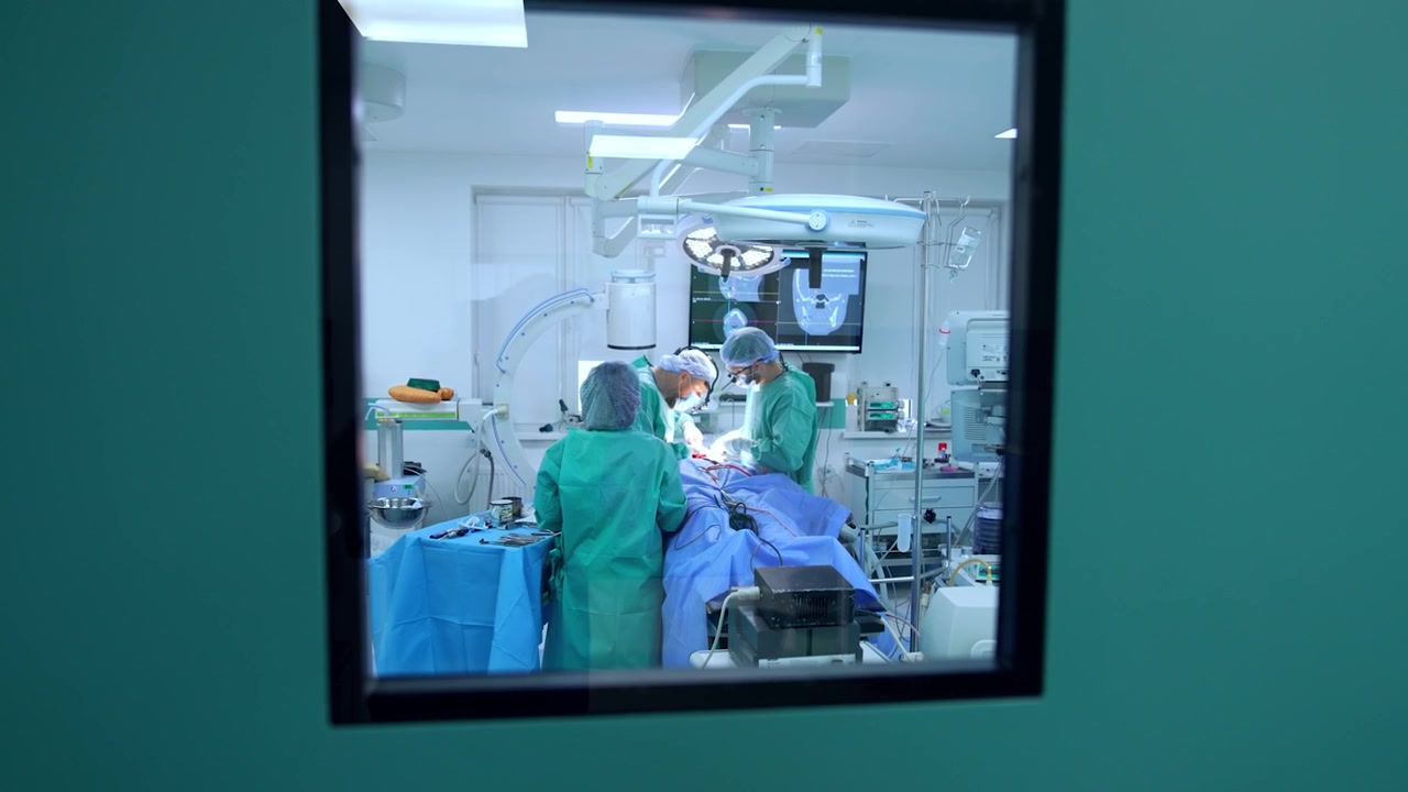 Interior of the modern well-equipped surgery room. Surgical operation is carried out in the operating theatre. View through the window in the door.