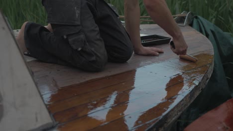 carpenter sealing bow of wooden boat deck with ultra violet protection varnish using roller