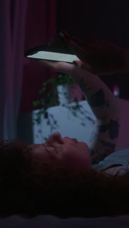 mujer acostada en la cama usando un teléfono inteligente por la noche