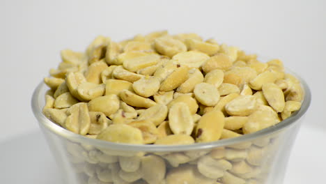 close up of salted peanuts in a glass jar rotating on a white background