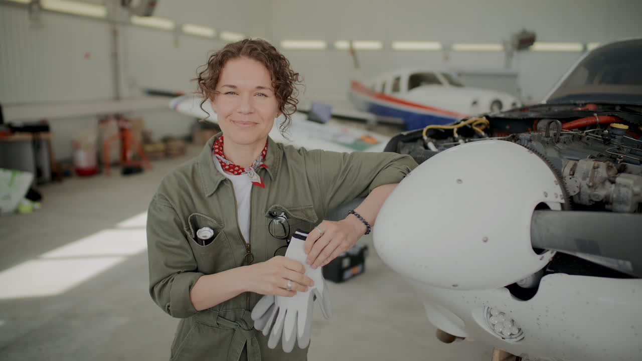 Portrait of Smiling Female Aircraft Mechanic Posing by Airplane in Hangar