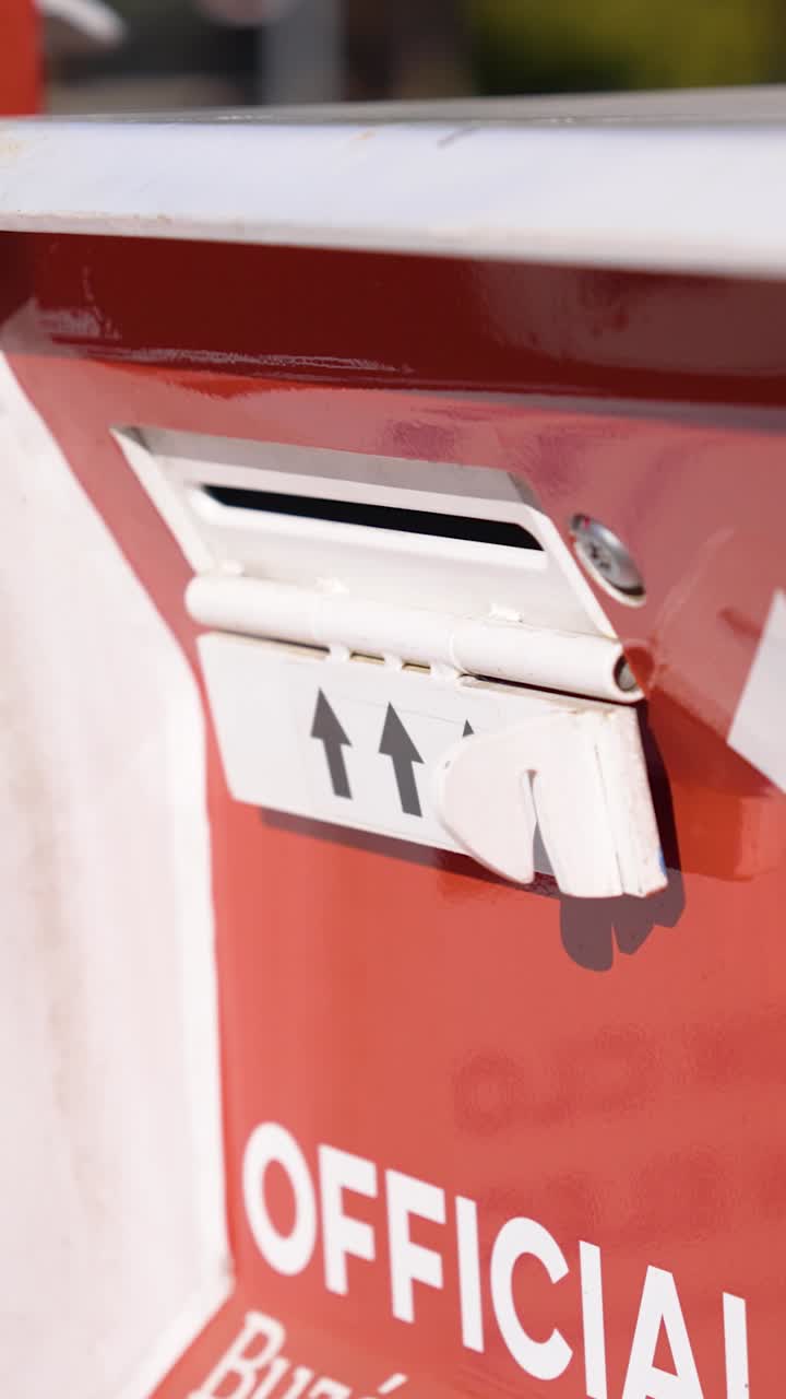 Vista verticale di una cassetta ufficiale per il deposito delle schede elettorali accanto alla segnaletica delle elezioni, che evidenzia l'accesso degli elettori, la raccolta delle schede e il processo di voto sicuro.
