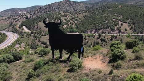 언덕 꼭대기에 있는 국가 상징인 스페인의 상징인 토로 데 오스본(toro de osborne)의 공중 전방 드론 전망, 일광