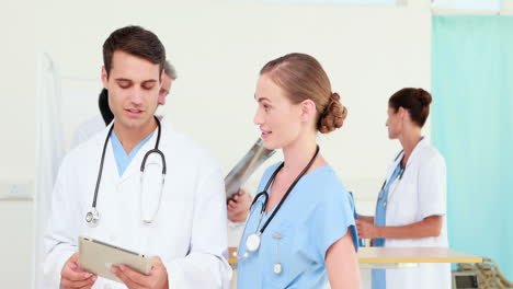 dos médicos mirando una computadora de tableta con sus colegas detrás