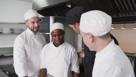 diverse male chef instructing group of trainee male chefs using tablet in kitchen, slow motion