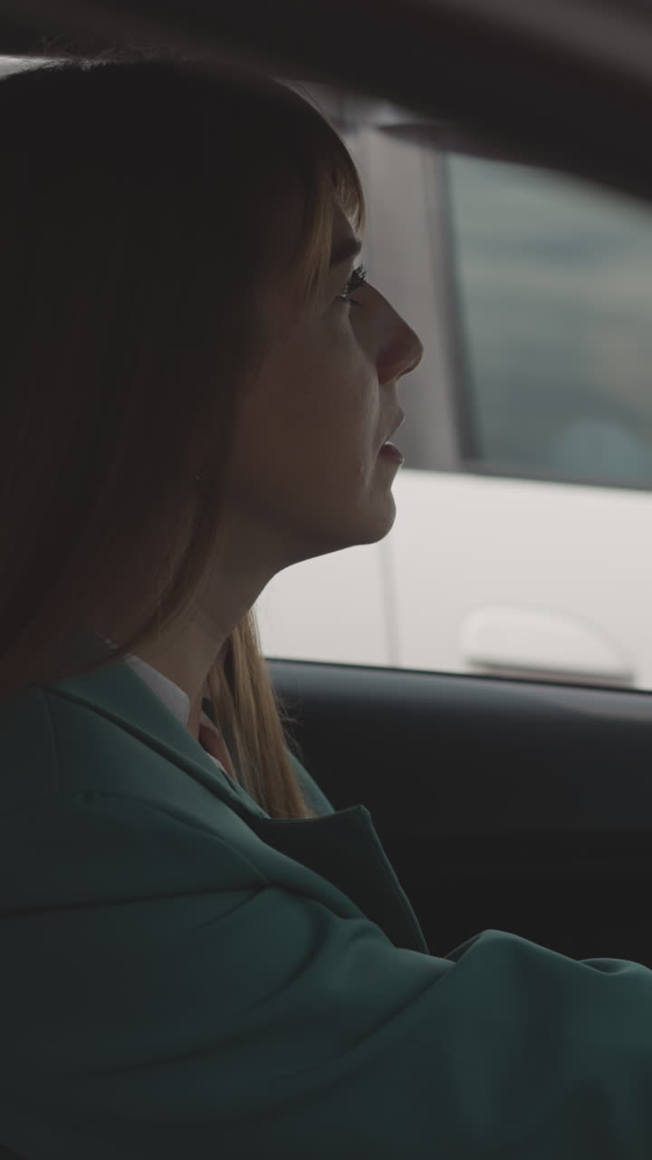 Focused woman puts hand on steering wheel on driver seat against passing car. Driver in green jacket sits in vehicle waiting out traffic jam cleared closeup