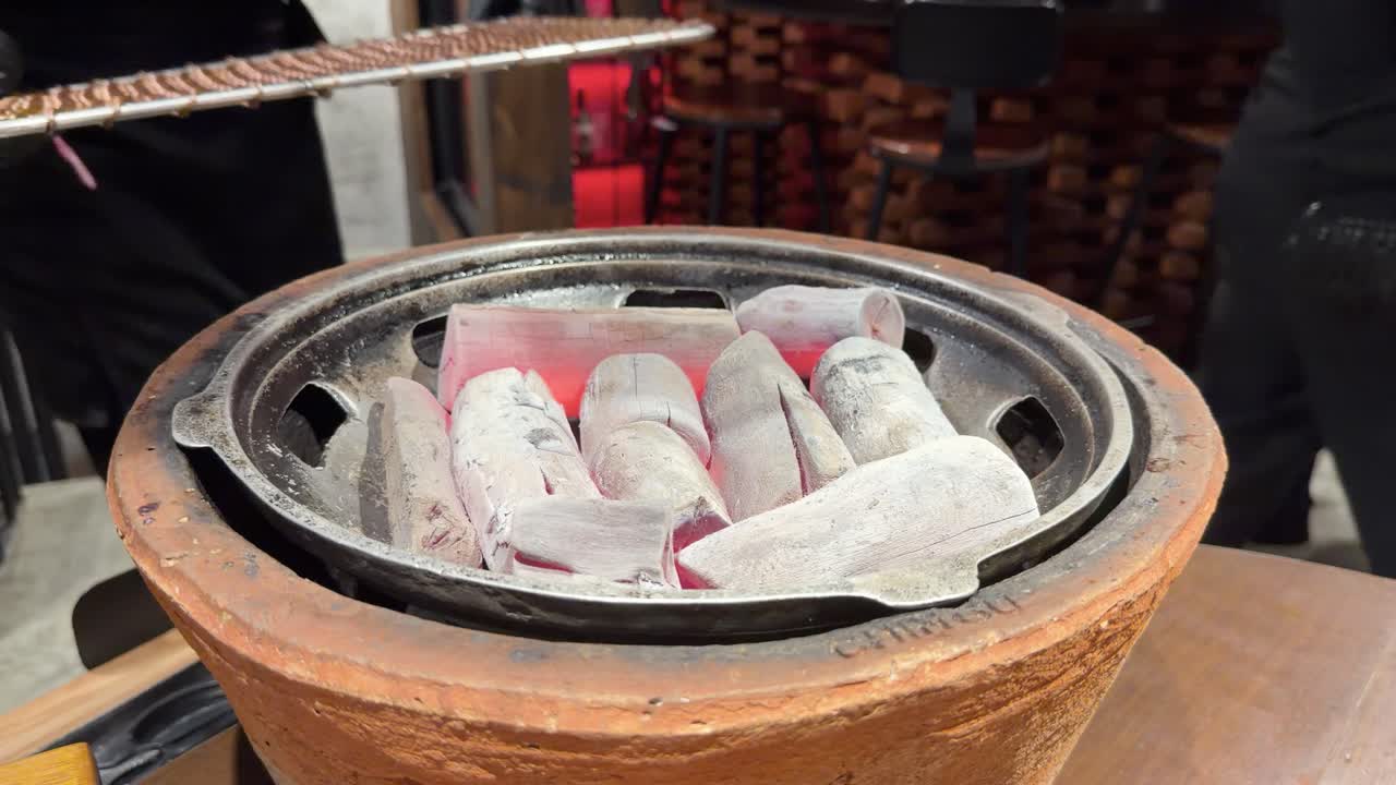 Gloved hands arrange hot charcoal, set grill grate, and cover with metal dome indoors