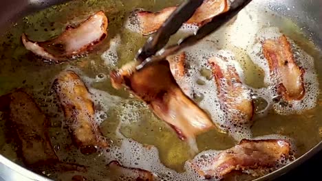 close-up of a slices of bacon being flipped on stovetop