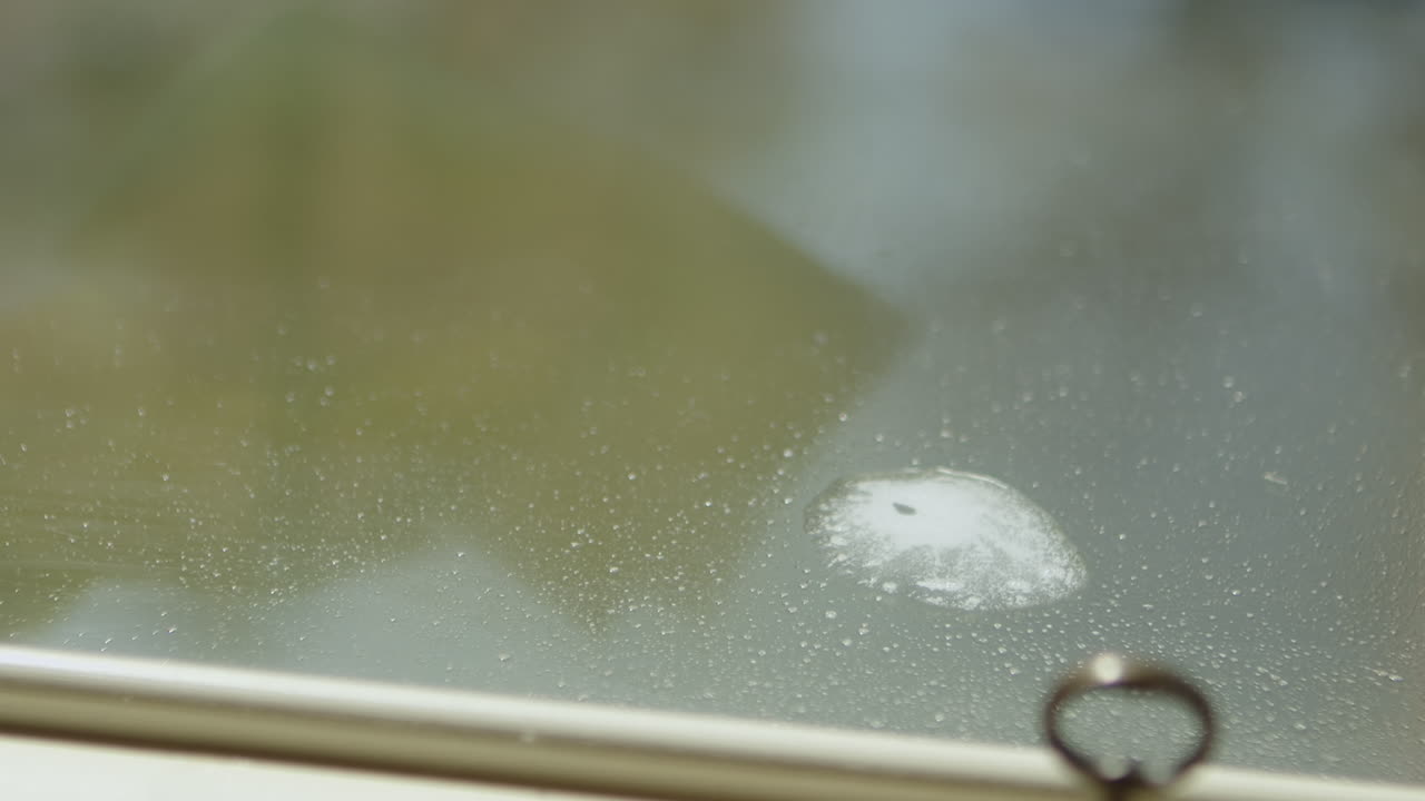 고무장갑을 끼고 있는 청소부의 손이 유리에 세척액을 뿌리고 와이퍼로 뿌립니다.