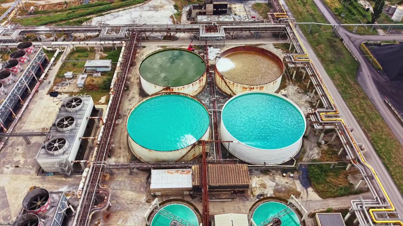 Water storage tanks at a waste management facility with different colored water during the day showcasing industrial activity