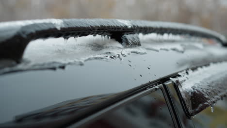 close-up of car roof covered in thick layer of ice and snow, featuring icicles hanging along edges of black metal rail. blurred wintery urban background