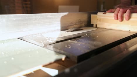 a woodworker rotates a piece of wood and pushes it over a table saw with multiple passes to make tenons from a piece of wood using a dado set in slow motion