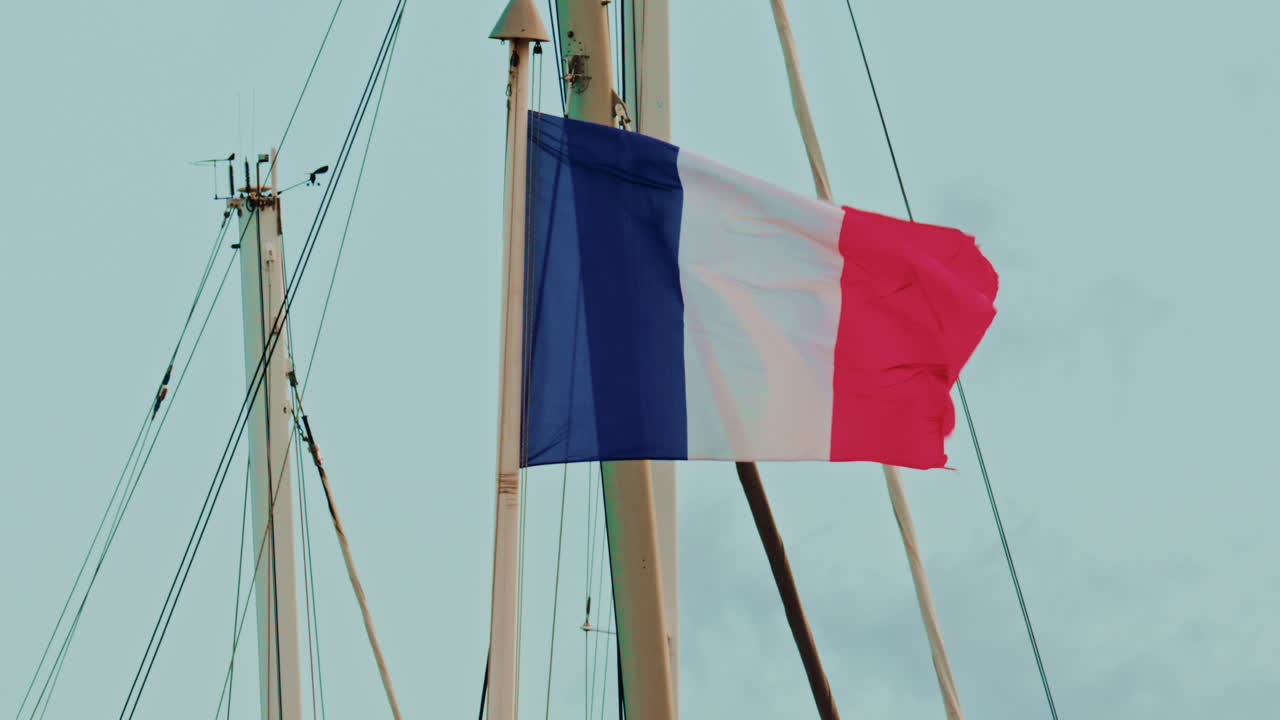 Close up of the French flag waving in the wind on a boat mast against a pale blue sky