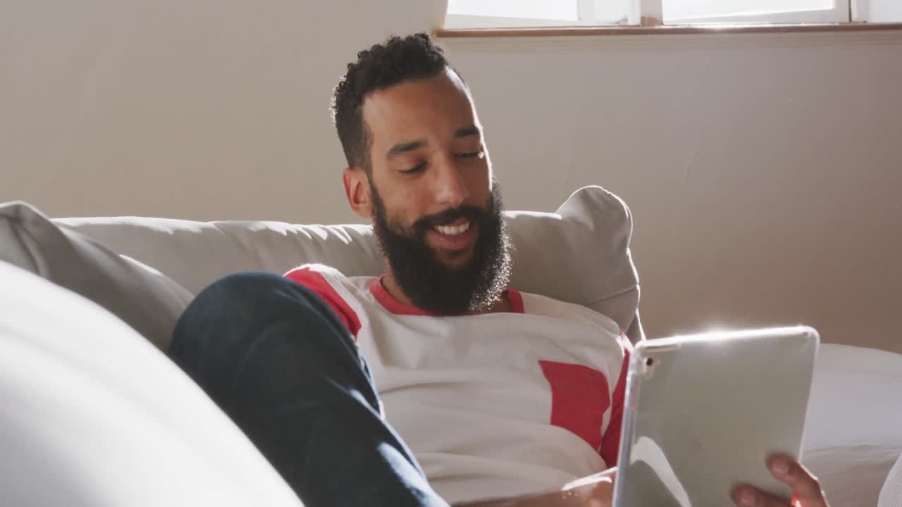 Handsome man smiling while using digital tablet on the couch