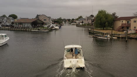 an aerial view of a fishing boat sailing through a canal behind houses on long island on a cloudy day