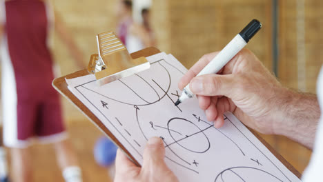 Hands-of-basketball-coach-drawing-diagram-on-clipboard