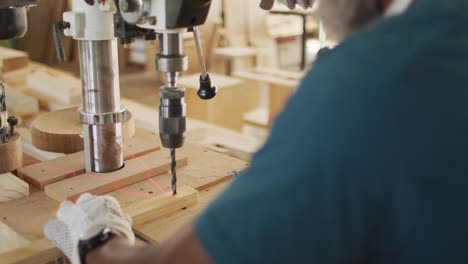 アフリカ系アメリカ人の男性木工が木工店でレーザードリルで木を掘っています