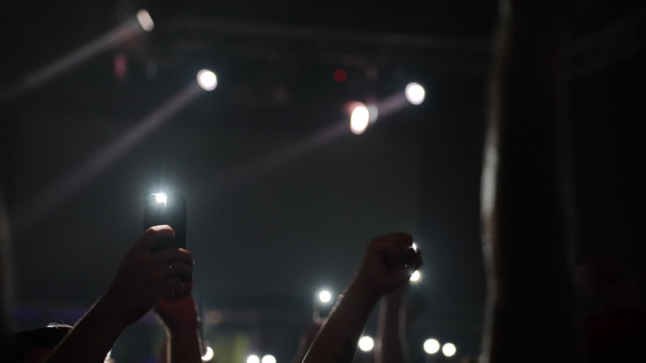 Mani alzate in segno di festa a un concerto vivace con luci brillanti e un'atmosfera energica.