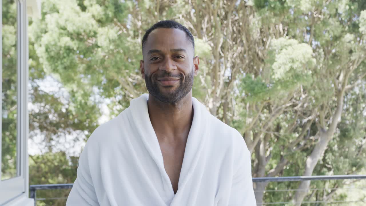 African American man on balcony wearing robe opening eyes smiling with sun warming face